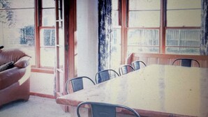 A room with a large window, a dining table with chairs, and a sofa. - Green Keepers Bach (Methven)