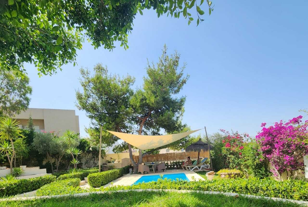 A pool area with a sunshade, surrounded by lush greenery and flowering plants.