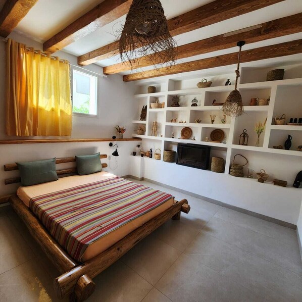 Une chambre confortable avec un lit en bois, une bibliothèque intégrée agrémentée d’objets décoratifs et un luminaire suspendu.
