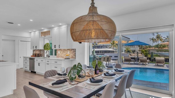 Una cocina moderna con armarios blancos, un comedor con vista a la piscina y una lámpara colgante grande de fibra natural.