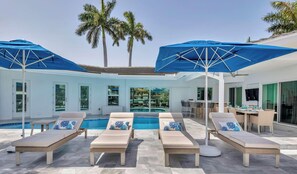 Un espace aménagé au bord de la piscine, avec des chaises longues, des parasols et une piscine.