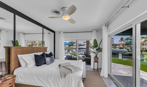 Une chambre Ă coucher avec un lit, un ventilateur de plafond, une grande fenĂȘtre et une vue sur lâextĂ©rieur.