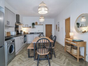 A compact kitchen with a dining area, a washing machine, and a large mirror. - No.7 Plas Darien (Holyhead)