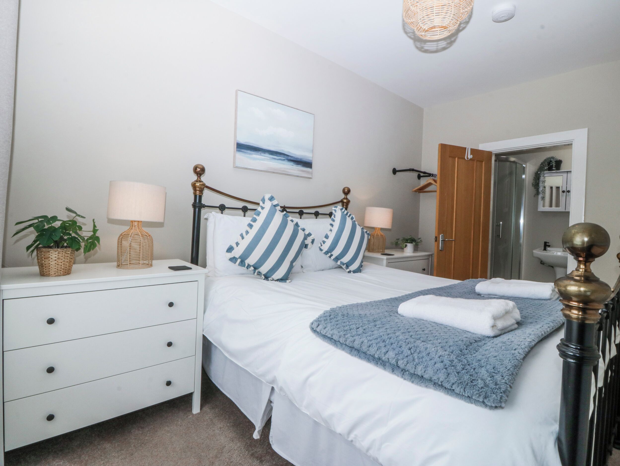 A neatly arranged bedroom with a bed, bedside tables, a hanging light fixture, a door, and a mirror.