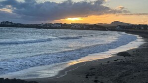 A coastal scene with waves, a beach, and buildings in the background. - No.7 Plas Darien (Holyhead)