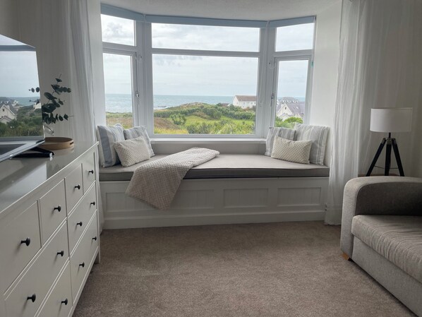 Una habitación con ventanal panorámico al mar, un aparador blanco, un sofá gris y una lámpara.