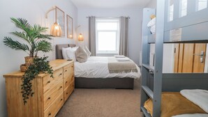 A bedroom with a bed, a wooden dresser, a potted plant, a window with curtains, and a bunk bed. - No.7 Plas Darien (Holyhead)