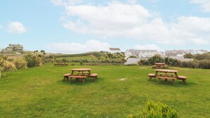 A grassy outdoor area with picnic tables and buildings in the background. - No.7 Plas Darien (Holyhead)