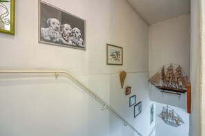 Un escalier avec une rampe, un tableau encadré représentant des chiots dalmatiens, une petite œuvre d’art encadrée et une maquette de bateau.