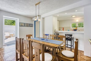 Een eetgedeelte met een houten tafel en stoelen, een keuken op de achtergrond en uitzicht op het omliggende landschap.