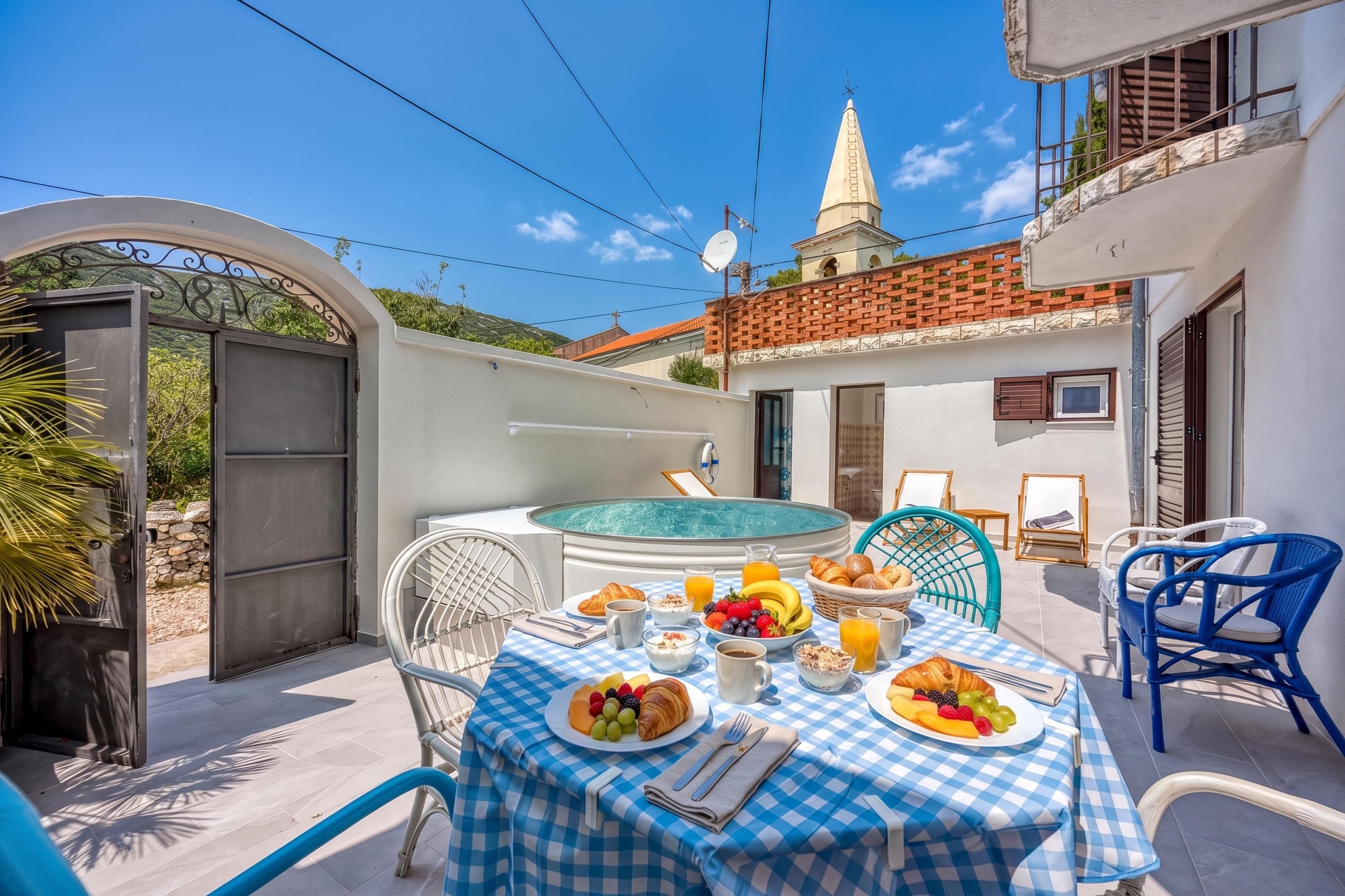 An outdoor dining area with a pool, a table set with breakfast, and a view of a church.