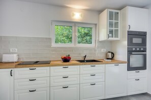 Una cucina moderna con mobili bianchi, un forno doppio, una finestra con vista e un piano di lavoro con un tostapane e una ciotola di frutta.