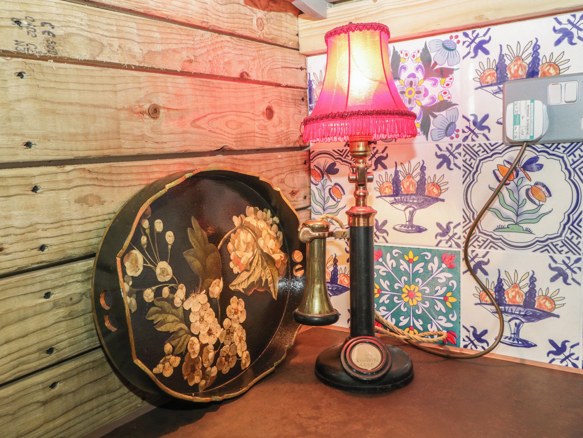 A wooden wall with a decorative plate featuring floral designs, a vintage-style lamp, and a tiled wall with colorful patterns.