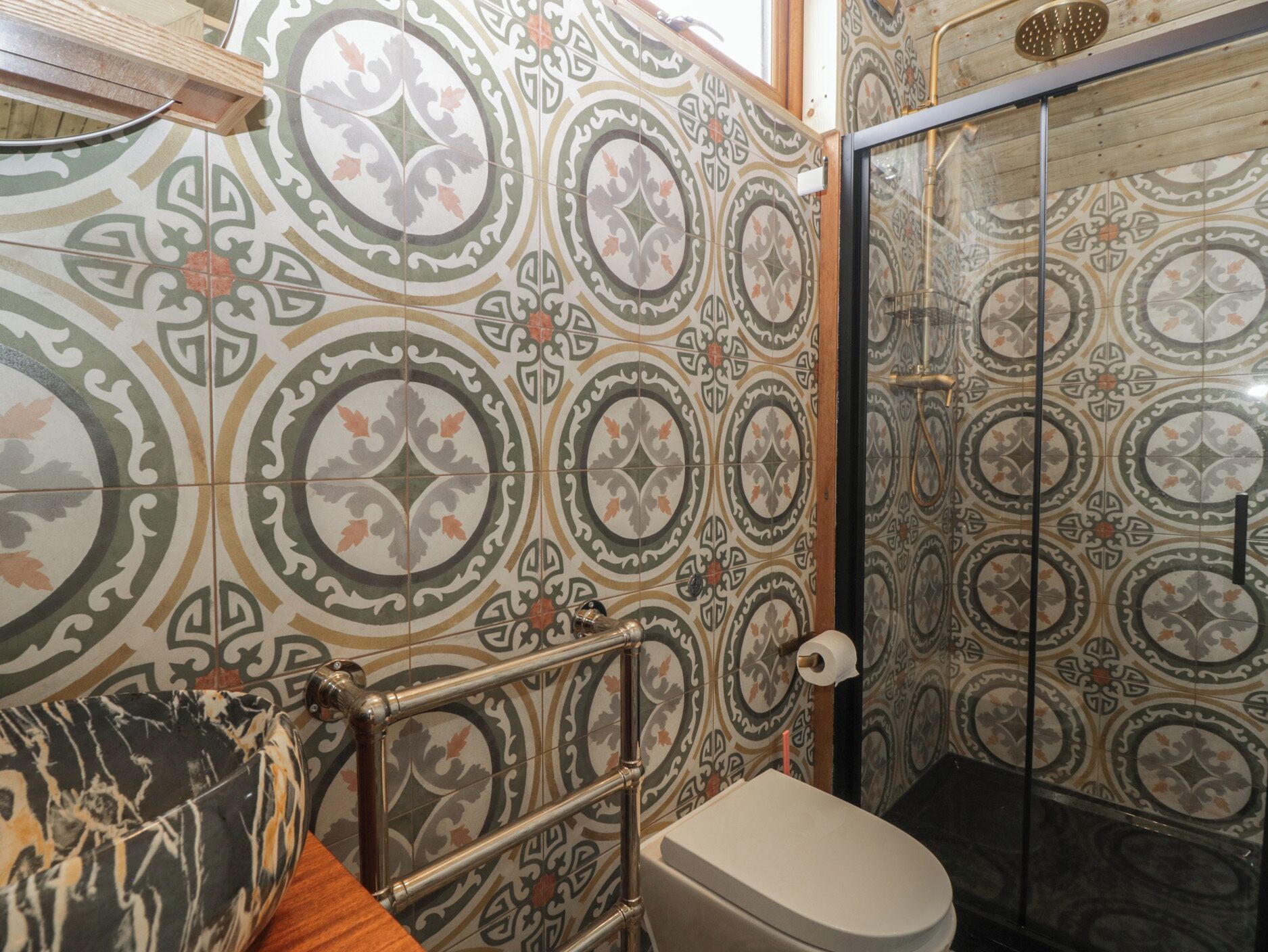 A bathroom with ornate tile patterns, a toilet, and a glass shower enclosure.