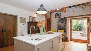 Una cocina moderna con una isla central, armarios de madera, un espacio para vinos empotrado y vista al jardín a través de una puerta de vidrio.