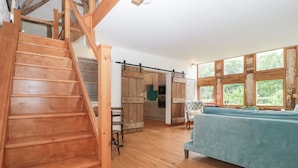 Una escalera de madera que conduce a un dormitorio entre pisos, con un ventanal y vistas al verdor.