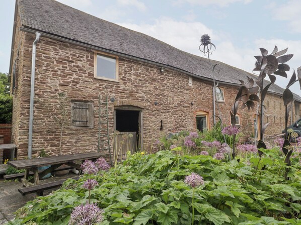 A stone building with a wooden door, a window, and a metal sculpture in the garden. - The Art House (Leominster)