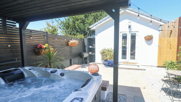 Un bain à remous sous une pergola en bois, avec un espace patio, un barbecue et des plantes en pot.