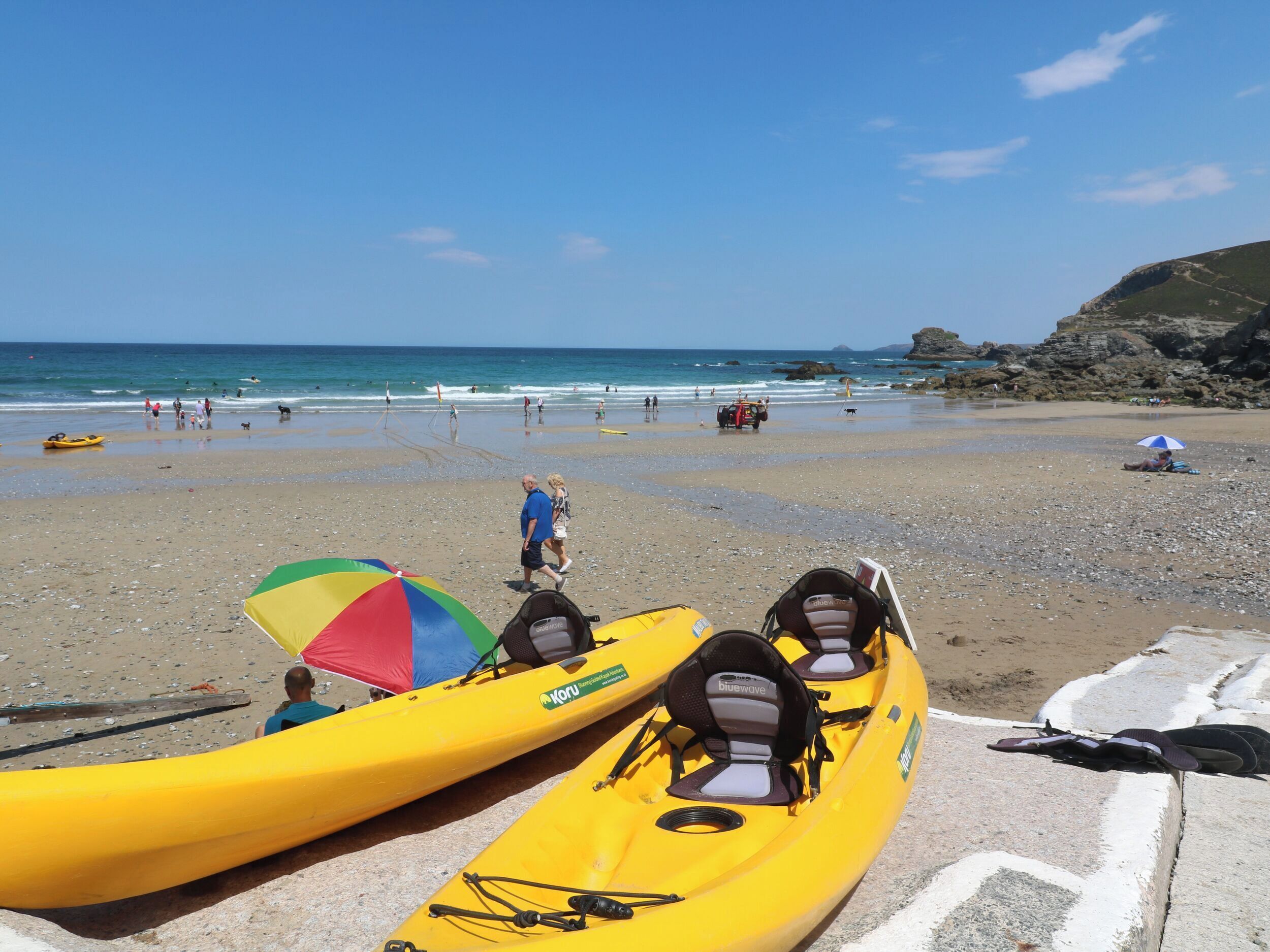 Une plage avec des kayaks, un parasol coloré et des falaises rocheuses en arrière-plan.