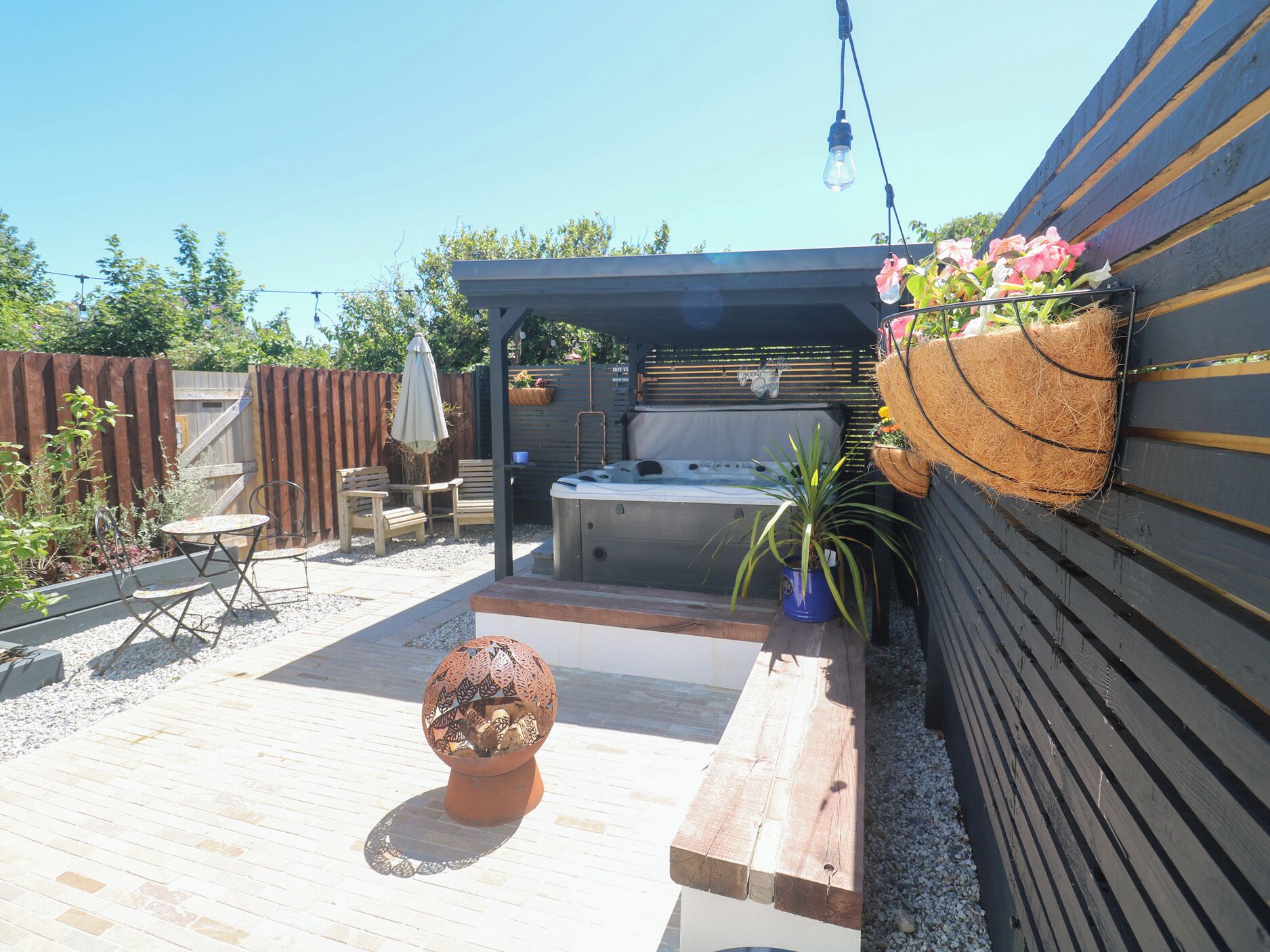 An outdoor patio area with a hot tub, seating, and a decorative plant.