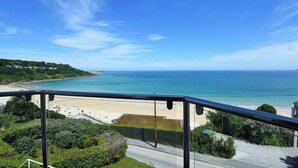 Une vue sur la côte depuis un balcon, avec un ciel dégagé, une plage et une route menant à la plage.