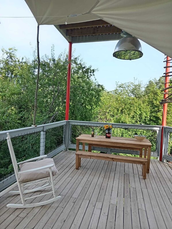 A wooden deck with a table and chairs, surrounded by a metal railing and a canopy.