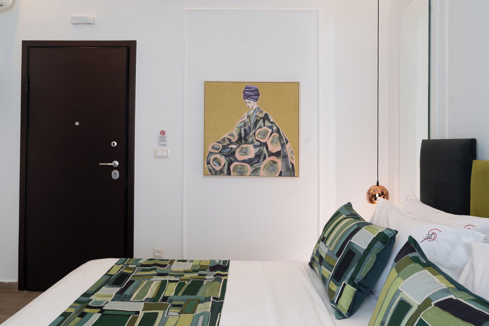Habitación de hotel con cama, puerta oscura, obra de arte colgada en la pared y lámpara.