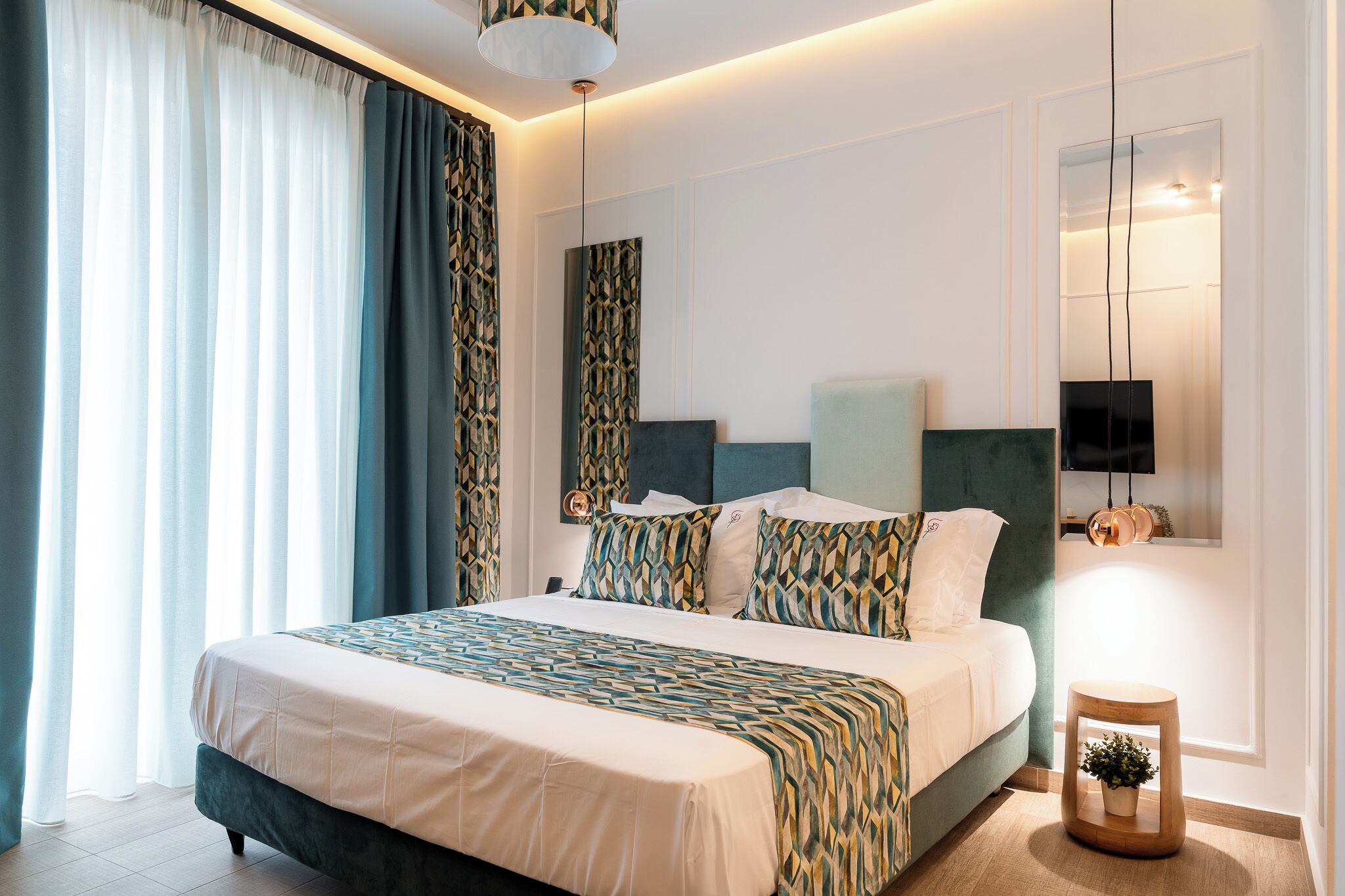 Una habitación de hotel moderna con una cama grande, una mesita de noche con una planta y un televisor montado en la pared.