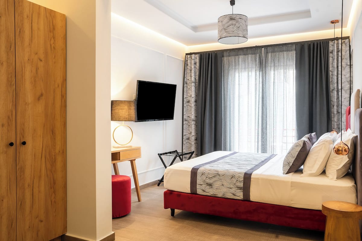 A modern bedroom with a large bed, a flat-screen TV, a desk with a lamp, and a wardrobe.