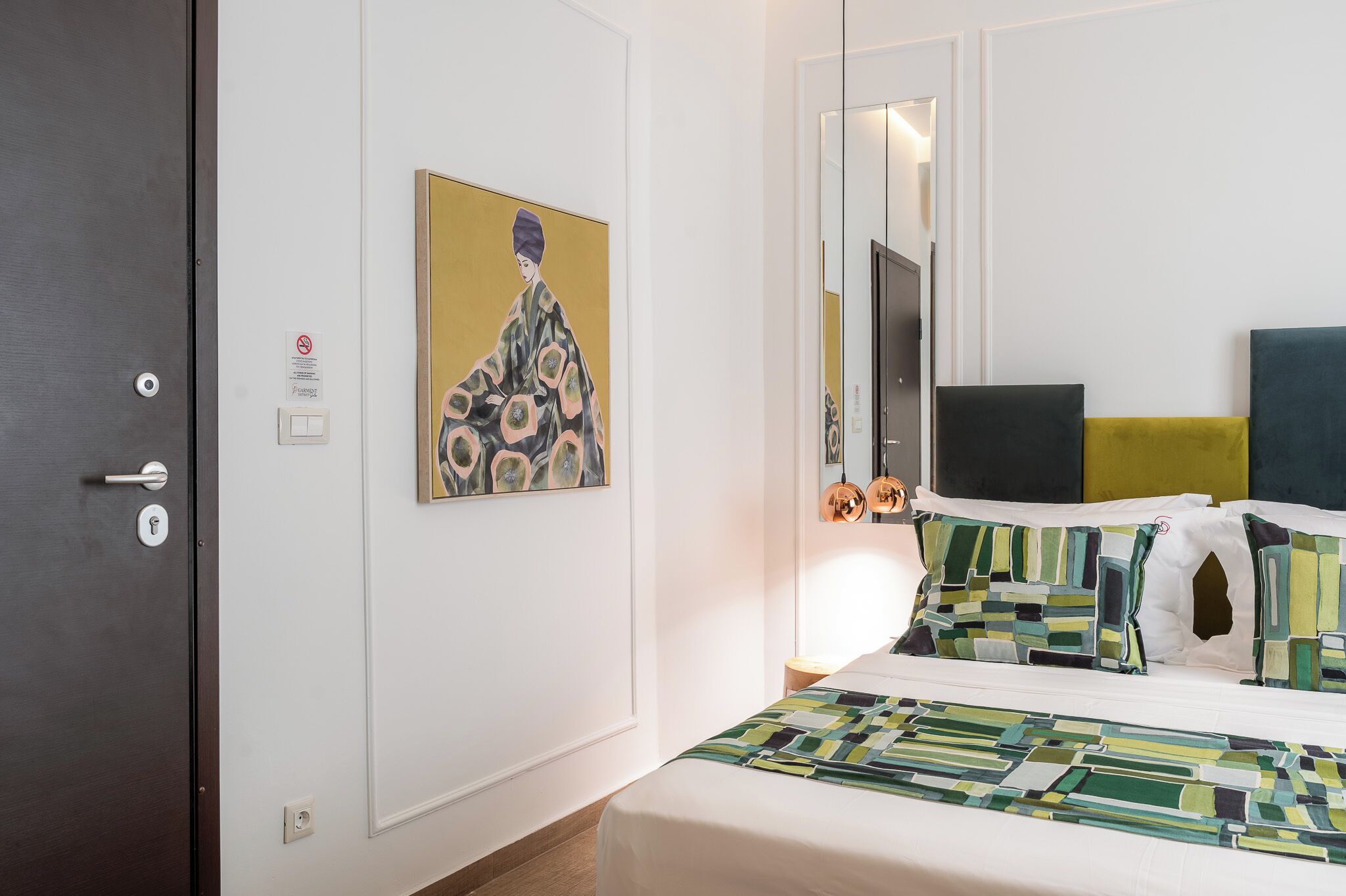 A hotel room with a bed, a painting, a television, and a door.