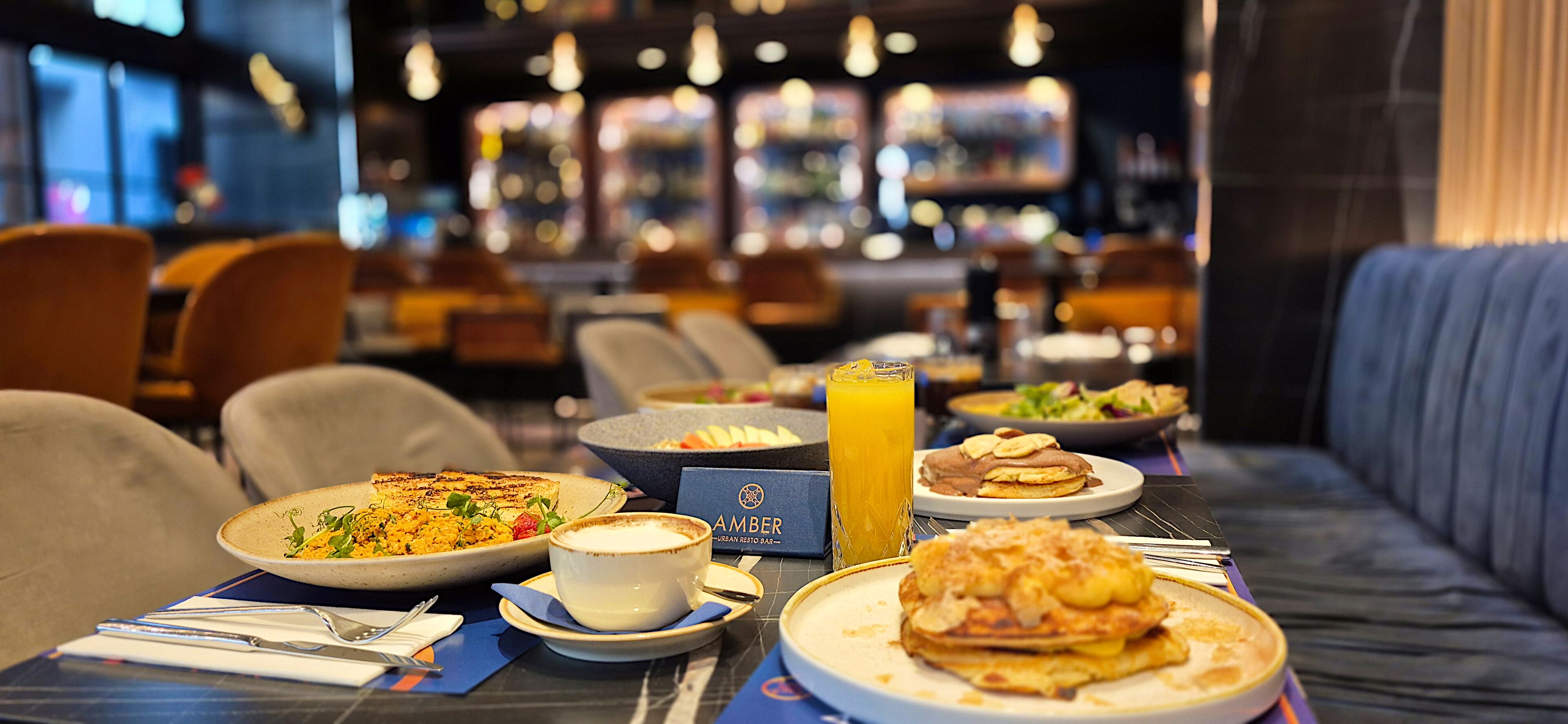 Un'ambientazione da ristorante con un tavolo apparecchiato per la colazione, comprensivo di piatti pieni di cibo, un bicchiere di succo d'arancia e un menu.