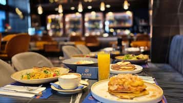 Un'ambientazione da ristorante con un tavolo apparecchiato per la colazione, comprensivo di piatti pieni di cibo, un bicchiere di succo d'arancia e un menu.