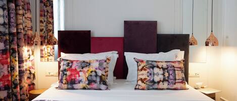 Una habitación de hotel con una cama, dos almohadas, una mesita de noche, una lámpara y cortinas.