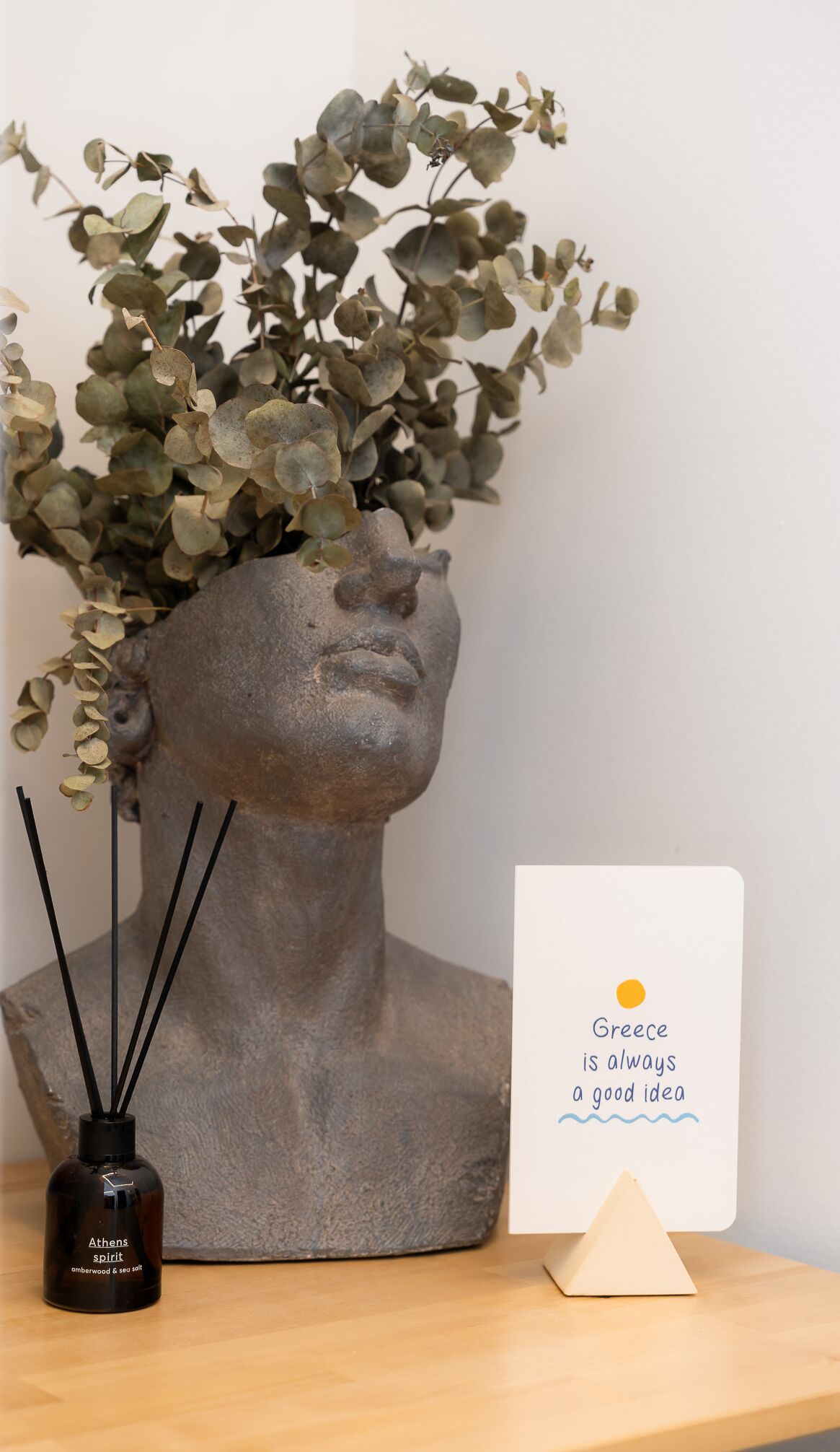 Una escultura de busto con una planta, una botella pequeña y una tarjeta con texto.