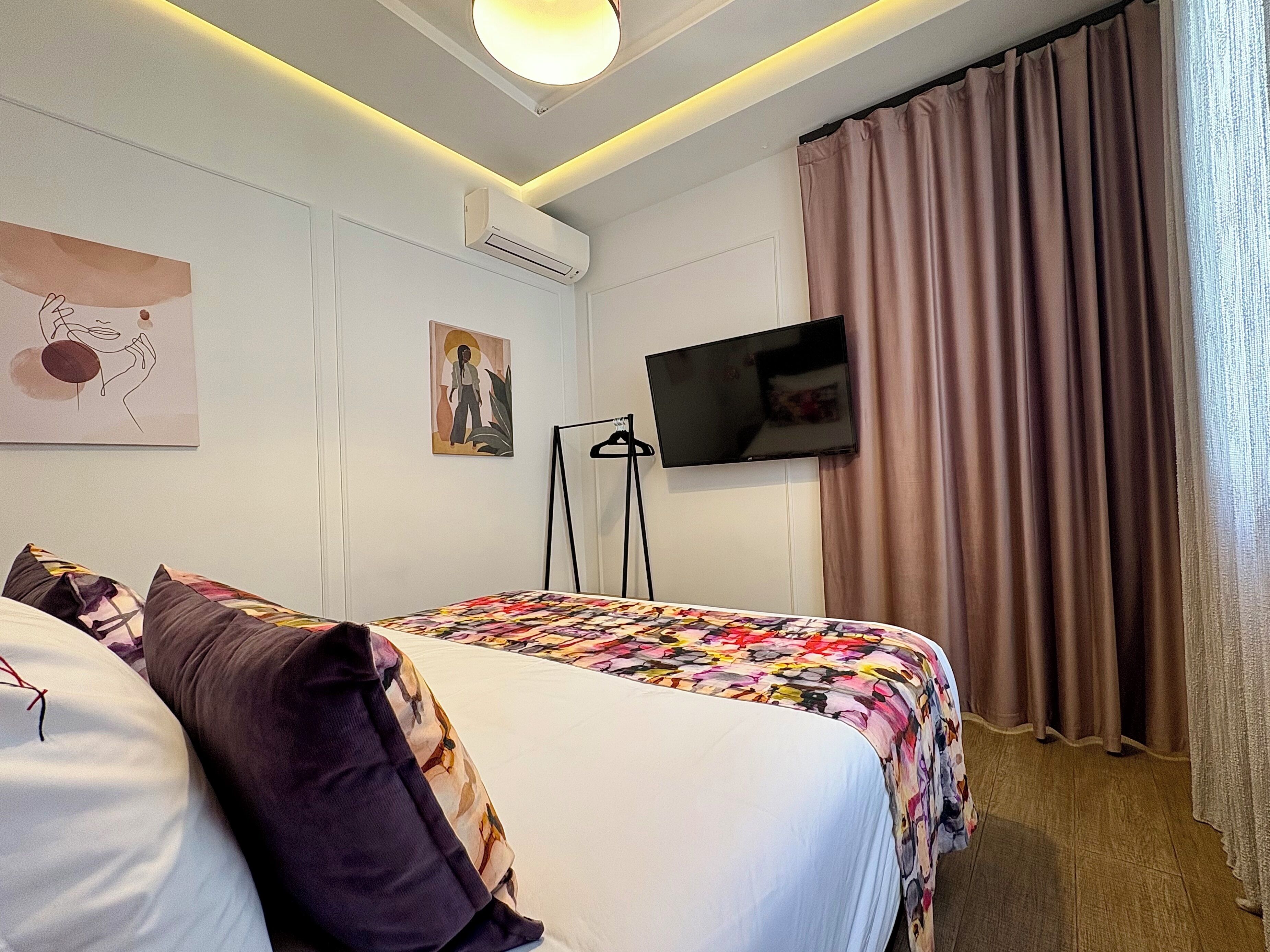 Habitación de hotel con cama, televisor de pantalla plana, un cuadro y ventana con cortinas.