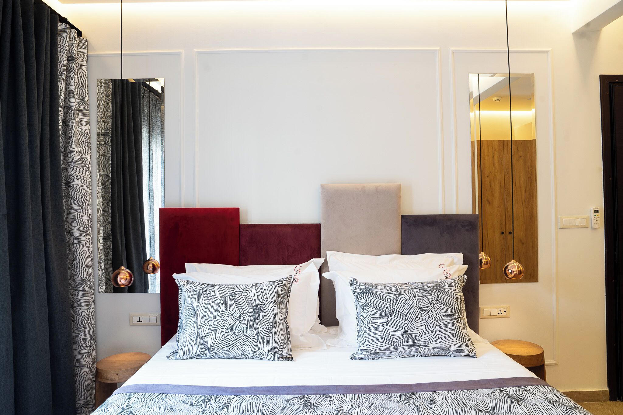 A neatly made bed with patterned pillows, a red headboard, and a mirror above it.