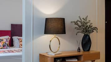 Un dormitorio con cama, mesita de noche, lámpara y un florero con plantas.