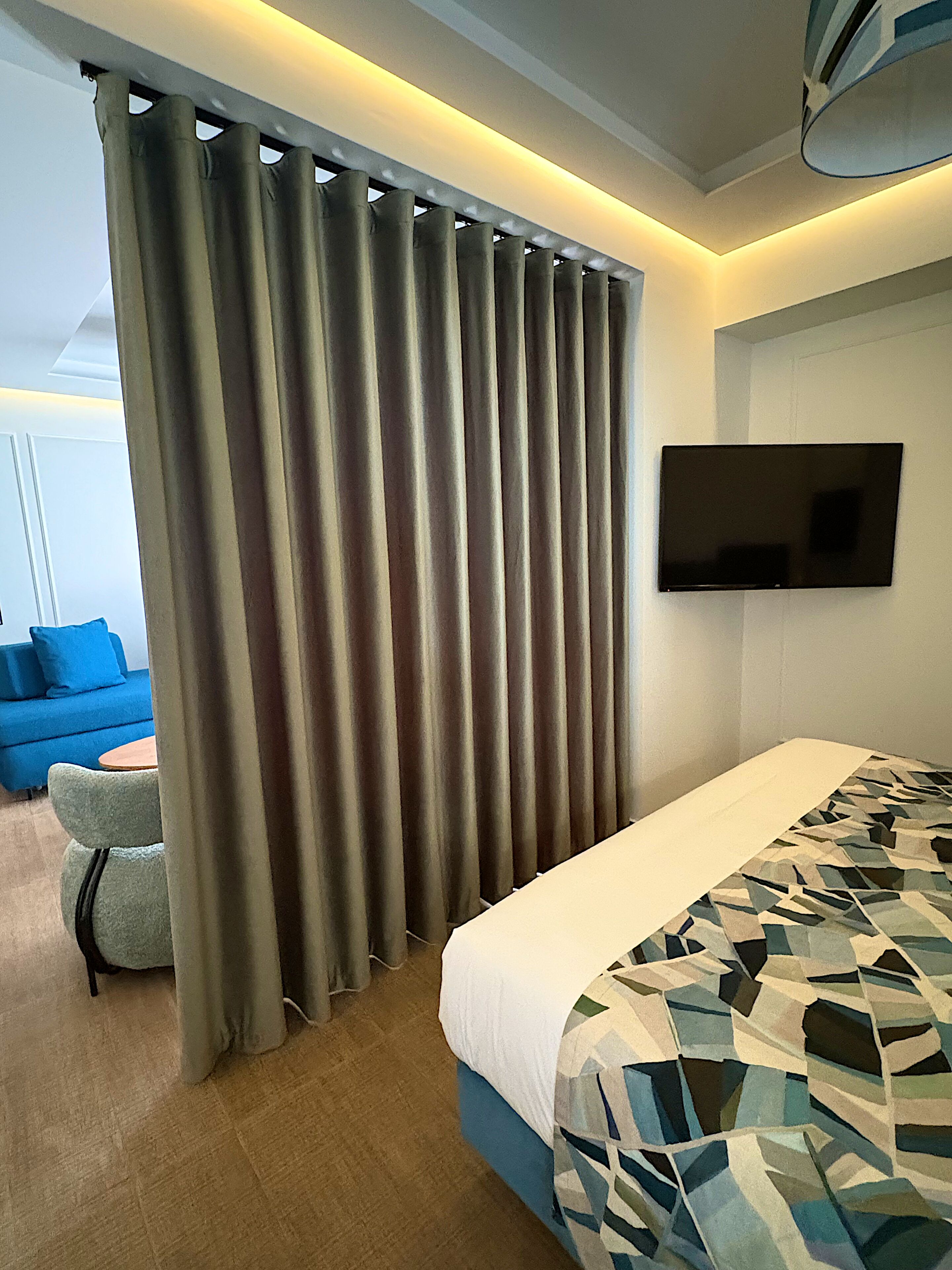 Un dormitorio con una cama, un televisor montado en la pared y una cortina.