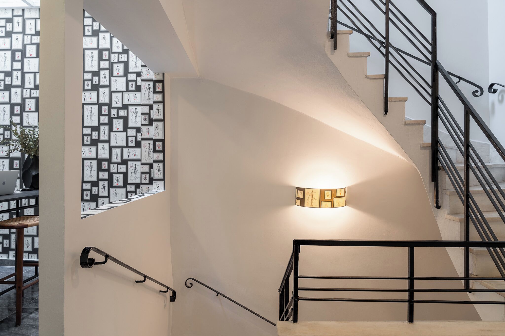 A staircase with a black railing, a wall-mounted light fixture, and a patterned wall with framed pictures.