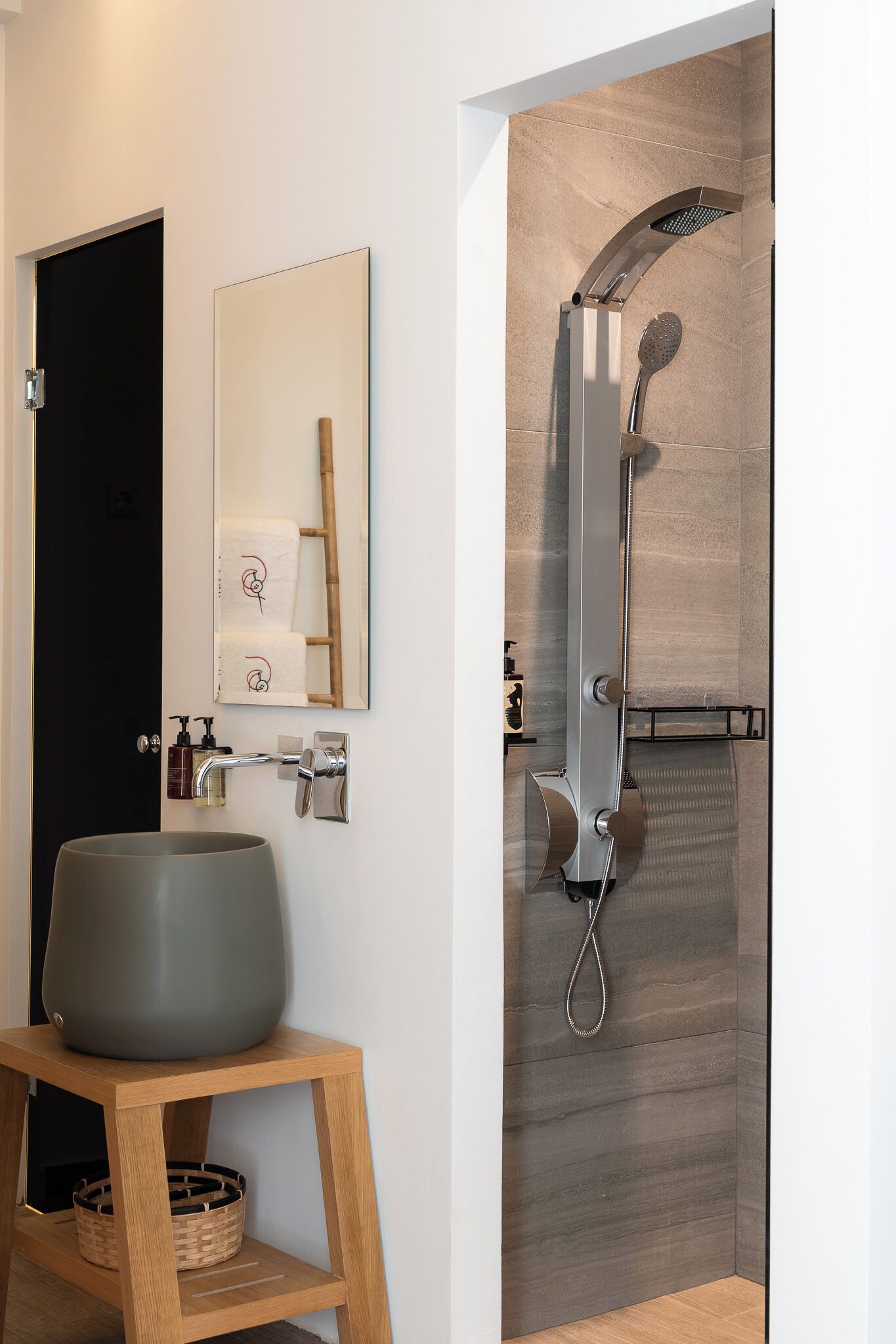 A modern bathroom with a large sink, a mirror, a shower, and a wooden stool.