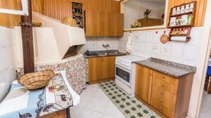 A compact kitchen with wooden cabinets, a gas stove, a sink, and a tiled floor. - Maria Catena House (Castiglione di Sicilia)