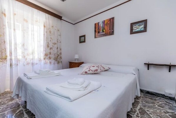 Habitación de hotel con cama, mesita de noche, lámpara y suelo de piedra.