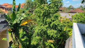 A residential area with a variety of vegetation, including banana trees and other greenery, alongside buildings with red-tiled roofs. - Kabera Bungalow Ubud (Ubud)