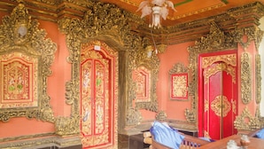 An ornate room with intricate golden decorations, red doors, and a chandelier. - Kabera Bungalow Ubud (Ubud)