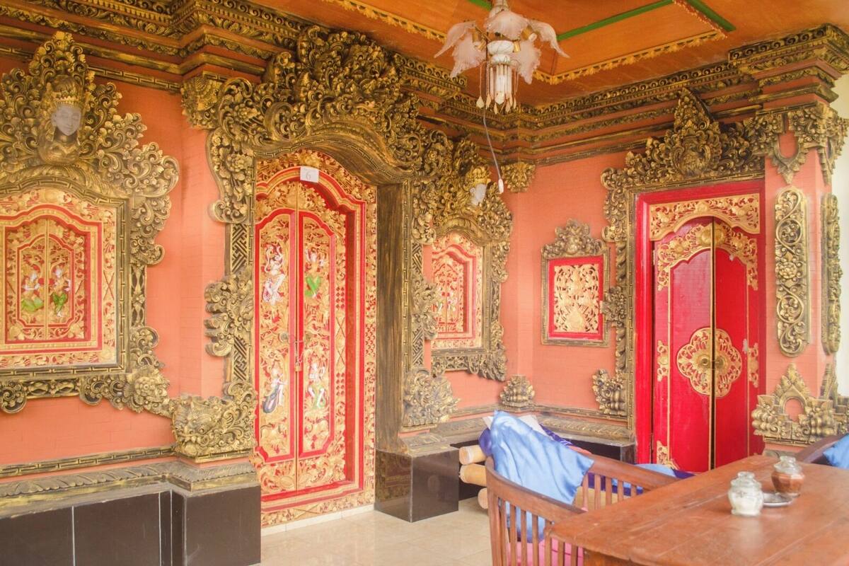 An ornate room with intricate golden decorations, red doors, and a chandelier.