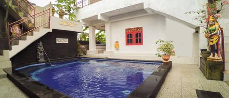 A swimming pool with a black border, a staircase with red railings, and a statue on the right.