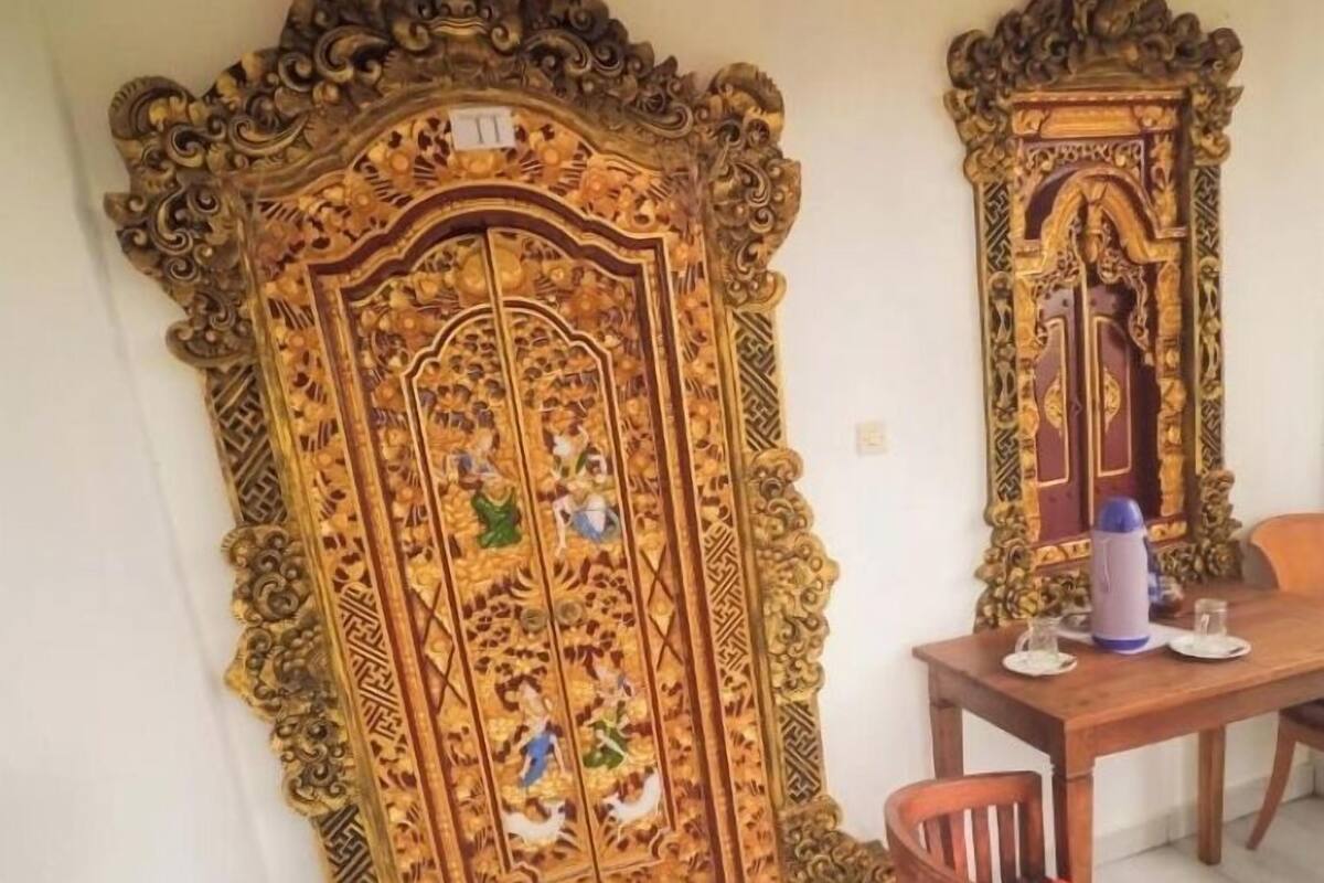 A dining area with a wooden table and chairs, a decorative door with intricate carvings, and a small trash bin.