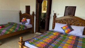 Two wooden beds with colorful quilts and pillows, a wooden headboard, and a tiled floor. - Kabera Bungalow Ubud (Ubud)