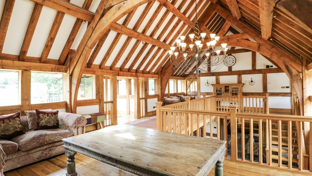 Una habitación amplia con techo de madera alto, una mesa de madera grande y una zona de estar acogedora con cojines estampados.