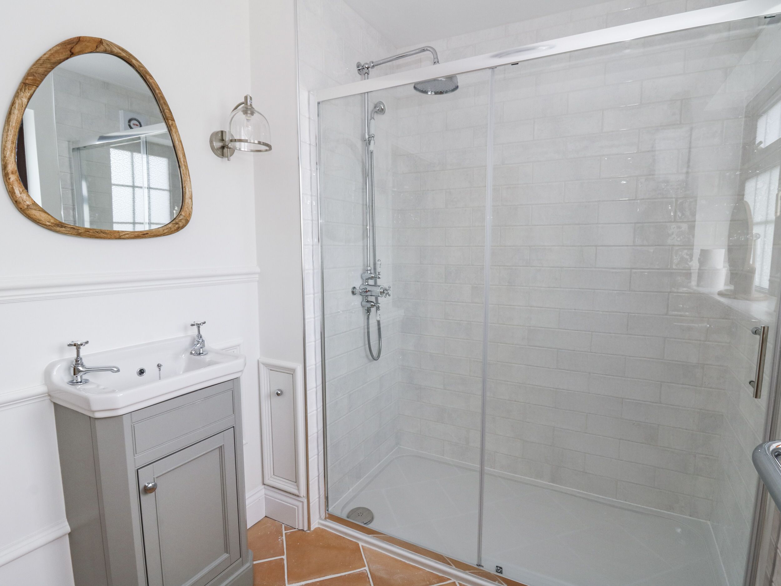 Un baño con ducha envuelta en vidrio, tocador con espejo y suelo de baldosas.
